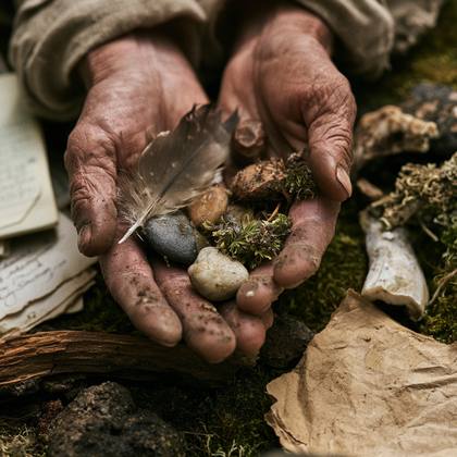 Cupped hands holding a feather, stones, and moss over old paper